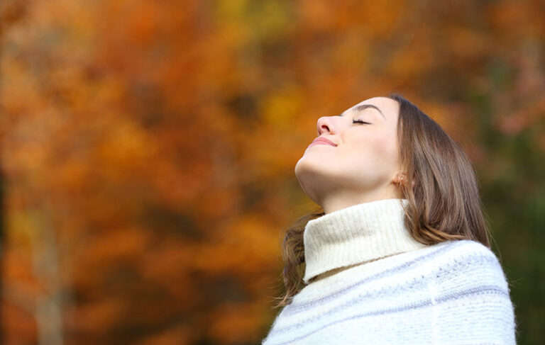 Eine schöne Frau im Herbstwald mit geschlossenen Augen, während sie tief einatmet und die Natur genießt.
